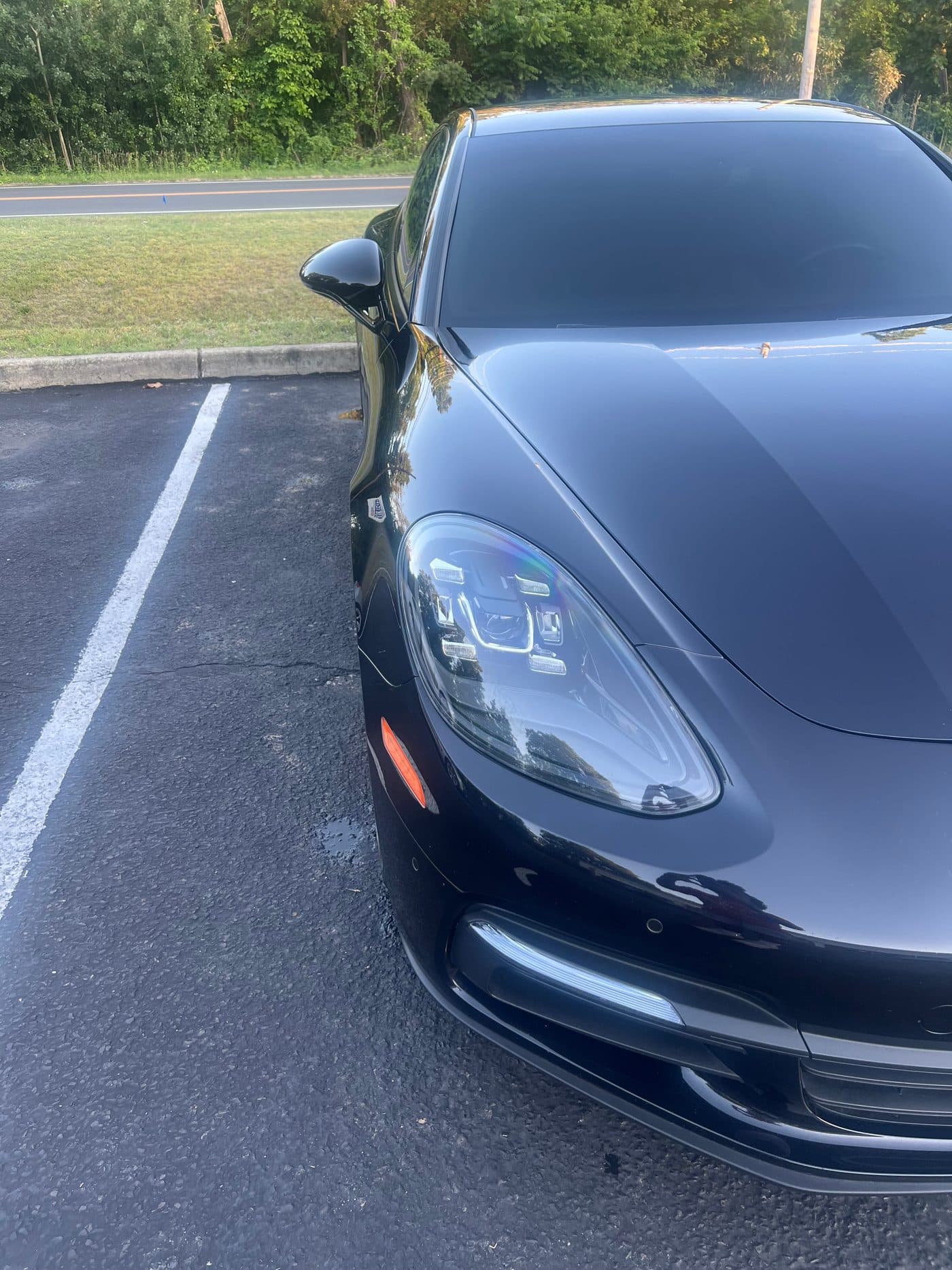 Glossy black Porsche Panamera front close-up showing headlight and hood after exterior detail