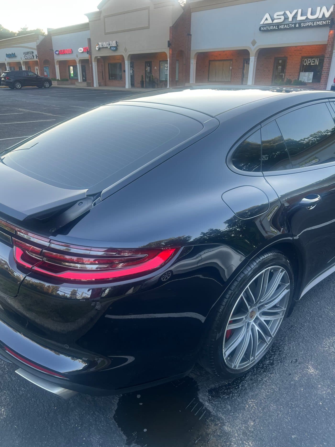 Gleaming black Porsche Panamera rear with glowing red tail lights and silver wheels